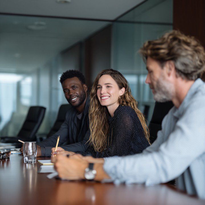 Three professionals in a modern conference room engaged in a collaborative business meeting, emphasizing teamwork and communication.