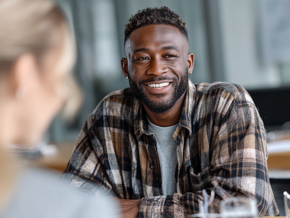 Portrait of a smiling businessman in a plaid shirt during a casual office meeting, representing positivity and workplace collaboration.