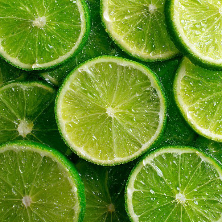 High-resolution close-up of fresh lime slices with glistening juice, arranged as a vibrant green citrus background.