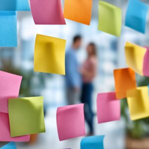 Creative brainstorming session with vibrant sticky notes on glass and blurred business people in the background.
