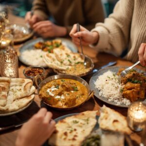 Close-up of a cozy dinner with friends sharing Indian food including naan, curry, and rice, symbolizing culture, warmth, and community.