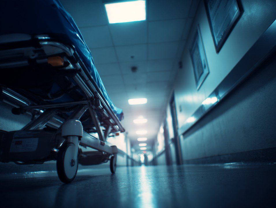 Close-up of a hospital stretcher in a dim, fluorescent-lit hallway, evoking urgency and emergency healthcare themes.