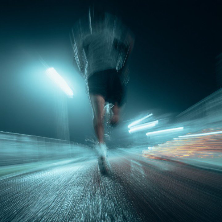 Motion-blurred athlete running on a rain-covered track at night under stadium lights, conveying speed and determination.