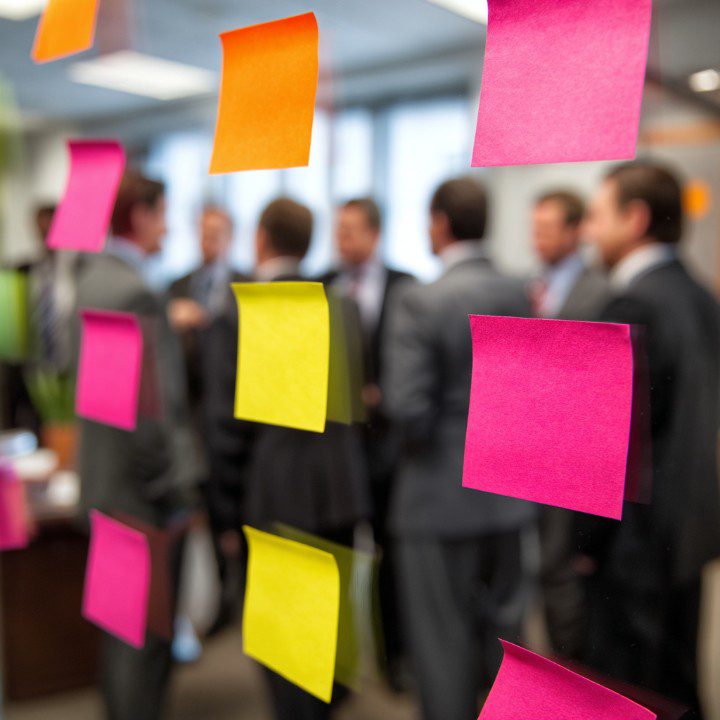 Business professionals in the background with colorful sticky notes on glass, illustrating teamwork and planning.