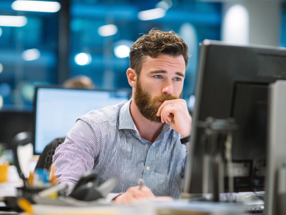Professional office worker concentrating on a desktop computer in a modern corporate environment with a focused expression.