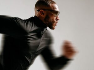 Side view of athletic man running in black sportswear with motion blur effect, symbolizing speed and performance.