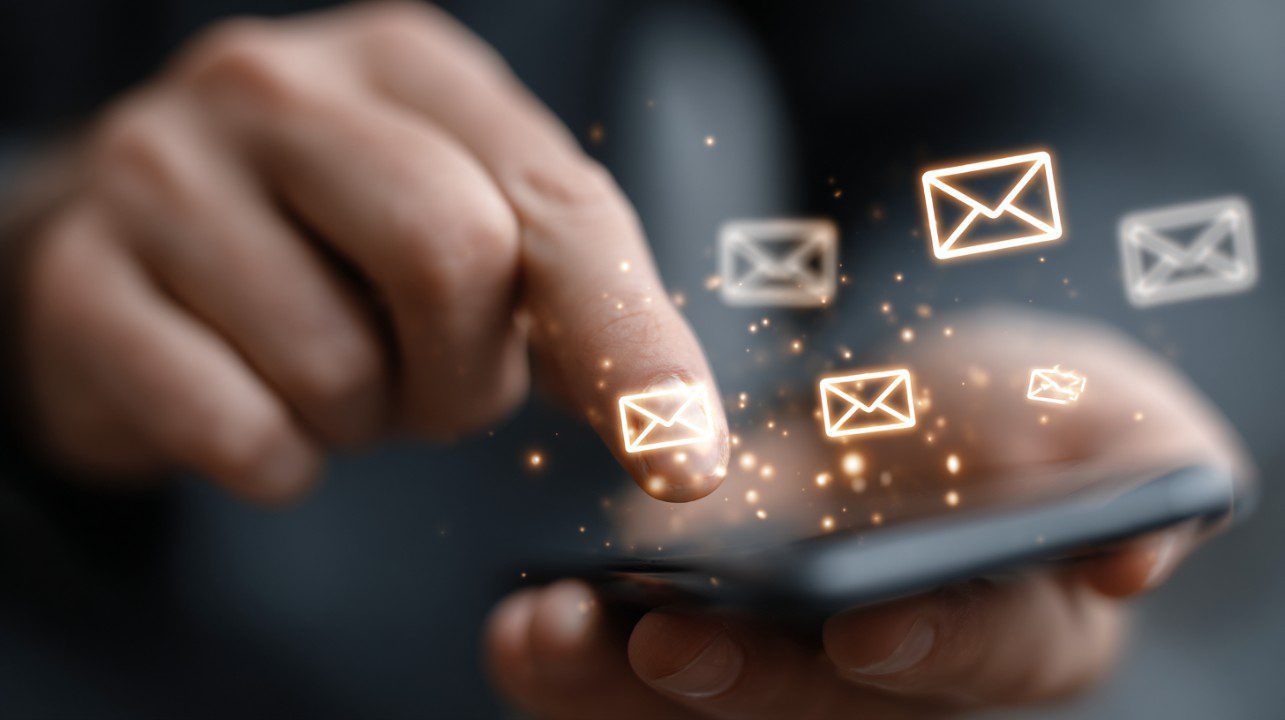 Close-up of a hand tapping a smartphone screen with glowing email icons floating above it, representing digital communication.