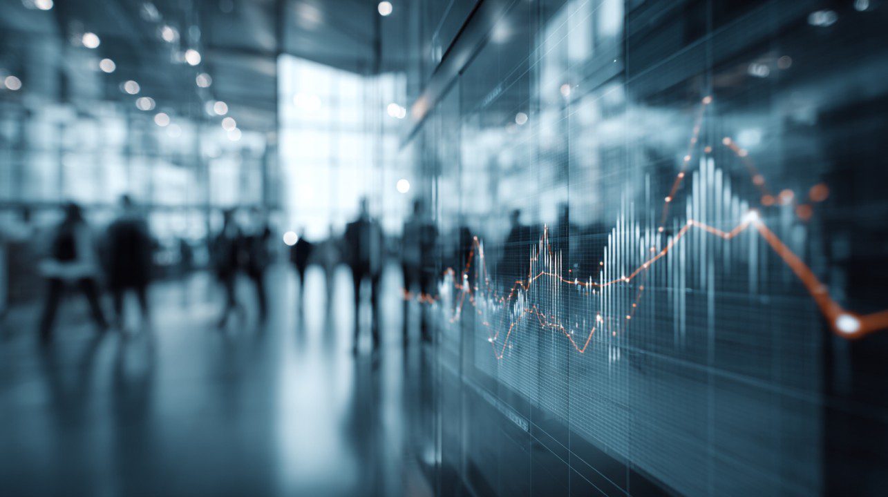 Blurred business office silhouettes with overlay of stock market graphs showing dynamic financial trends.