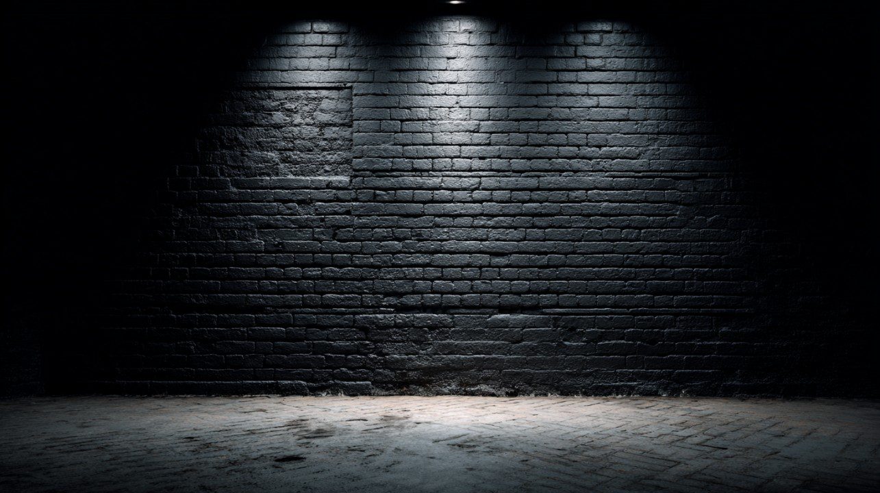 Black painted brick wall illuminated by three overhead spotlights in a dark theater, with a spotlight effect on the floor creating a dramatic scene.