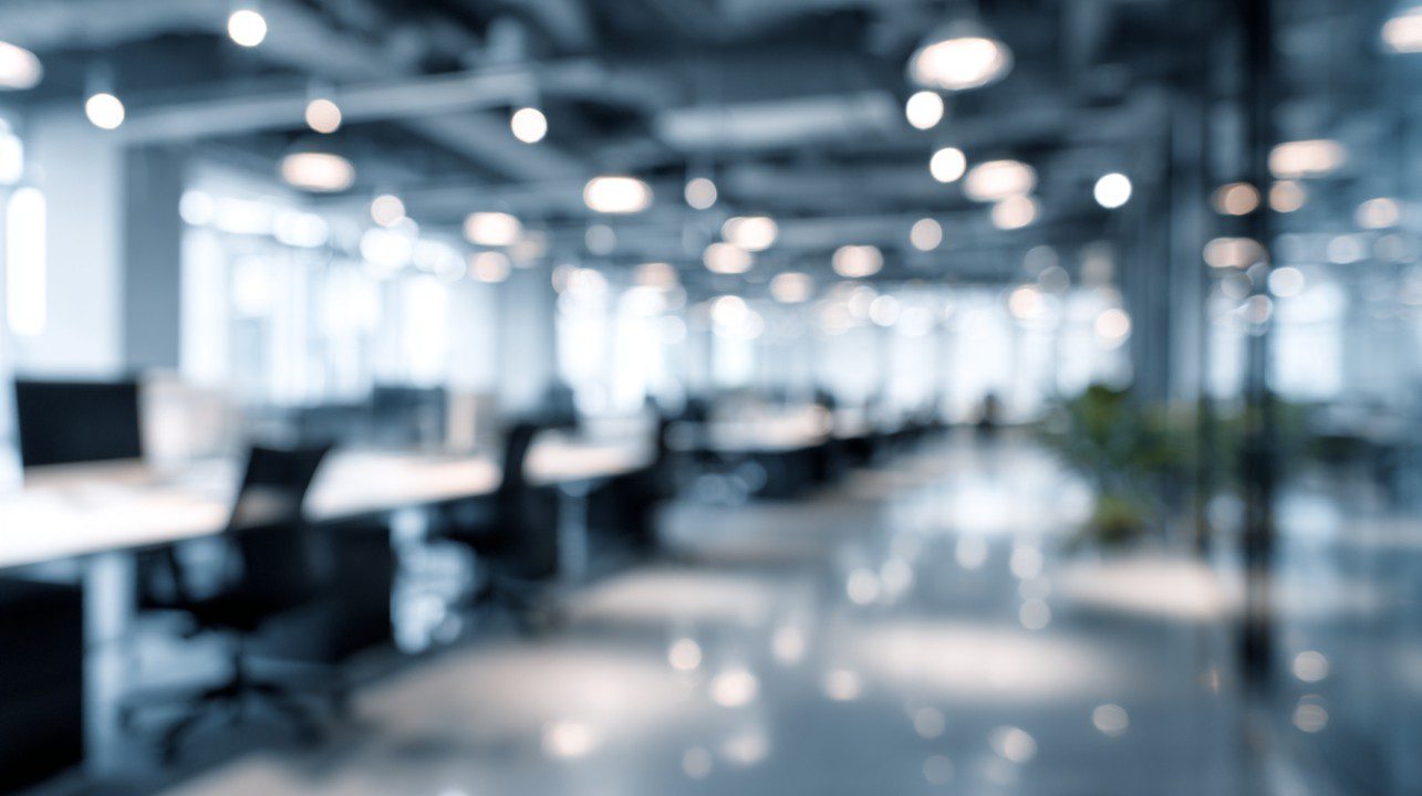 A blurred image of a spacious open office with modern furnishings in blue-grey tones, ideal for business presentation backdrops.