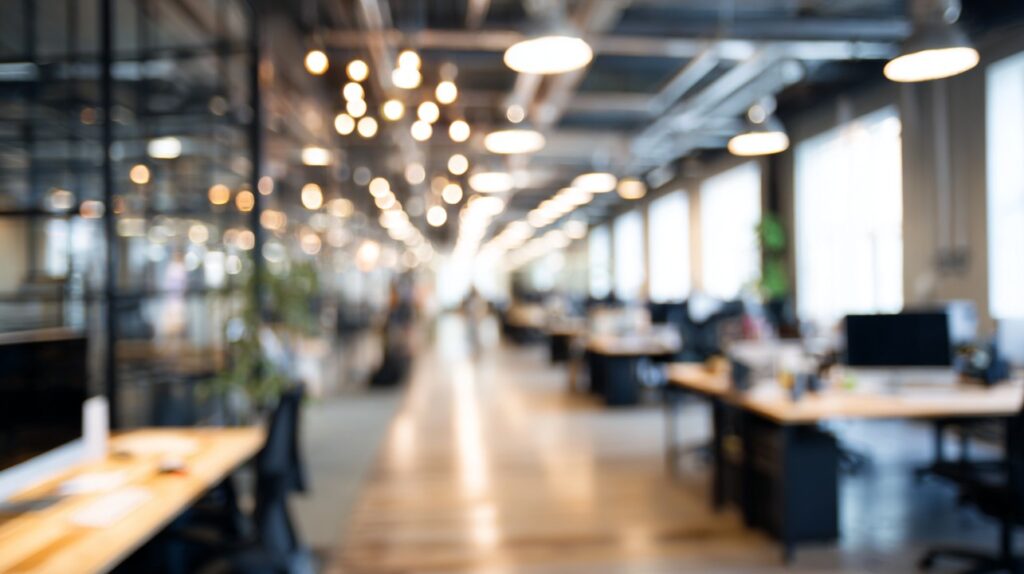 Bright modern office space with warm ceiling lights, blurred background, and wooden desks creating a welcoming work environment.