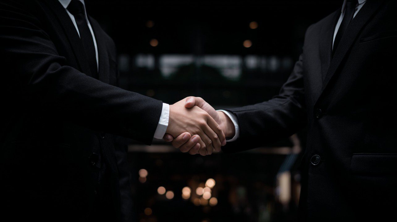 A close-up handshake between two professionals in dark suits, representing trust, business partnership, and corporate agreement.