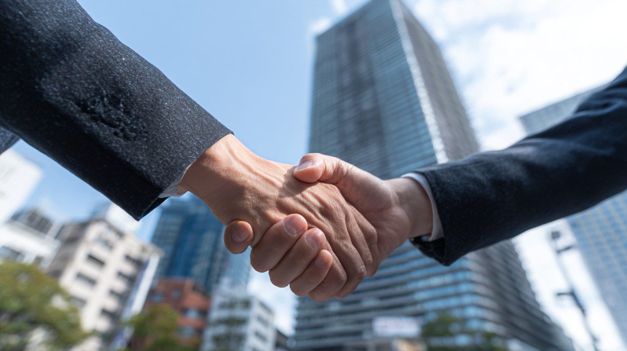 Two professionals shaking hands with modern skyscrapers in the background, symbolizing corporate success and partnership.
