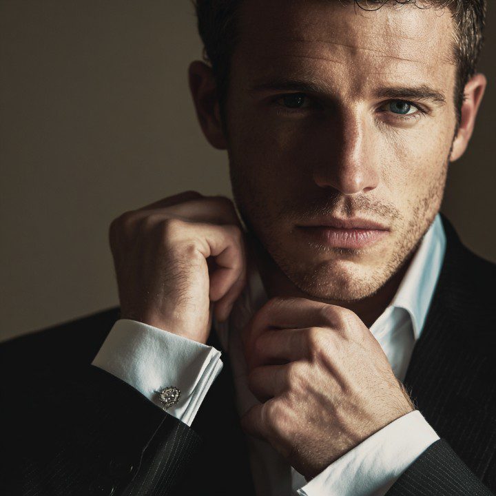 A confident man in a dark suit adjusting his collar, captured in a moody, close-up portrait ideal for leadership or fashion content.
