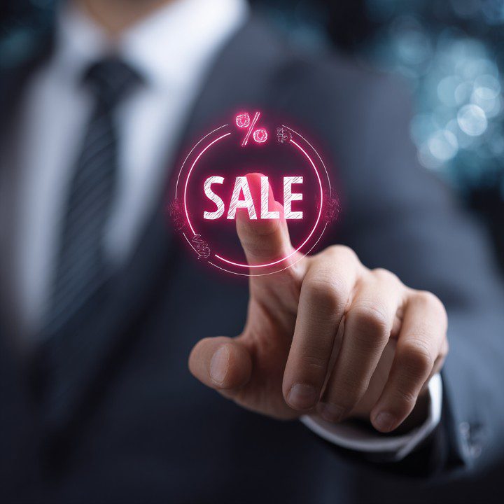 Businessman in suit pointing at glowing pink sale icon symbolizing marketing and discounts.
