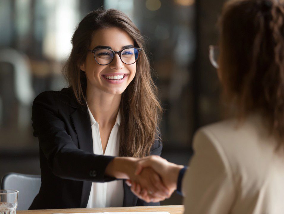 Young businesswoman with glasses smiling and shaking hands during a professional business meeting.