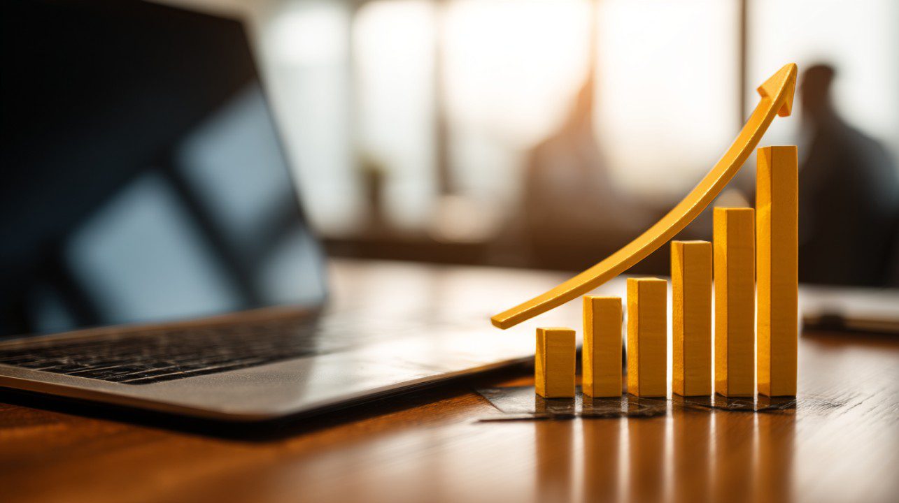 Realistic image of a financial team working with digital tools and a yellow rising bar graph on a wooden desk symbolizing growth.