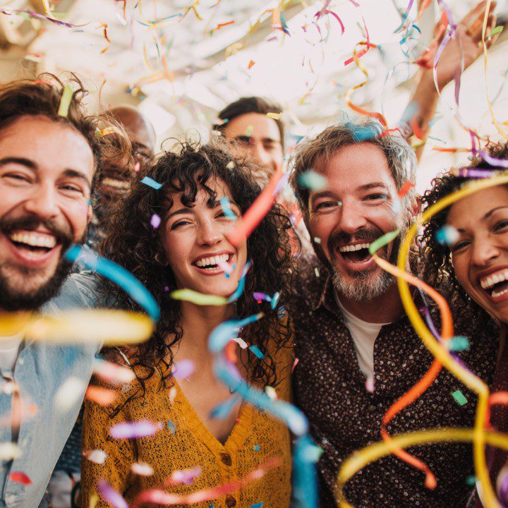 A cheerful group of diverse people smiling and laughing during a celebration with colorful confetti falling around them.