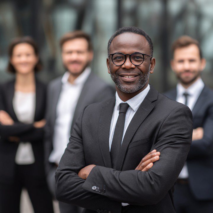 Confident insurance team leader wearing glasses and suit, with a professional team blurred in the background.