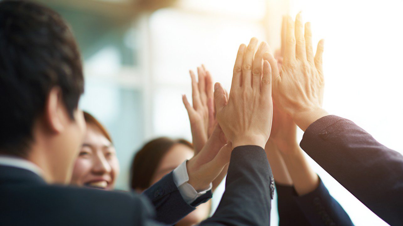 Close-up of Korean office workers joyfully giving a group high-five in a bright office.
