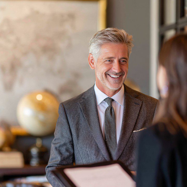 Smiling mature businessman in a gray suit engaged in conversation in a professional office environment.