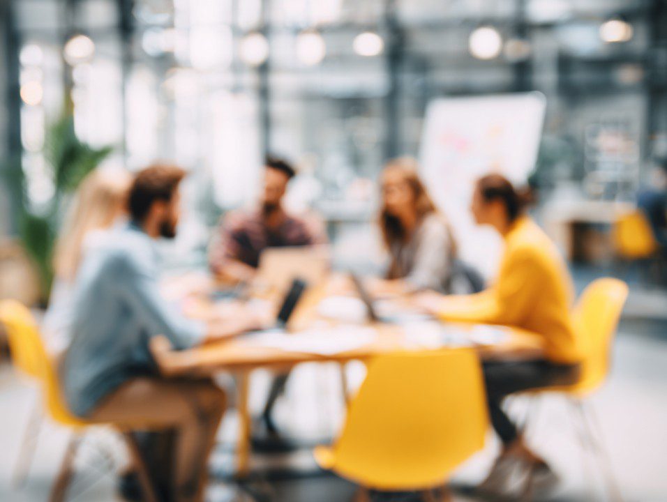 Modern business team in discussion with blurred background in a bright office, highlighting teamwork and collaboration.