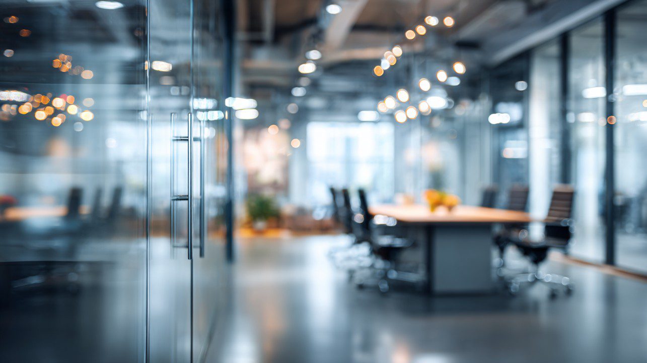 Blurred modern office interior with glass walls, conference table, and warm lighting, perfect for corporate and business backgrounds.