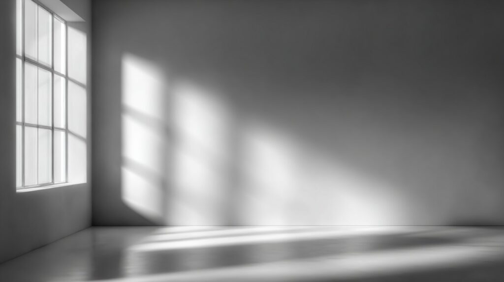 Black and white photo showing a plain white wall with soft light and window shadows creating a minimalist atmosphere.