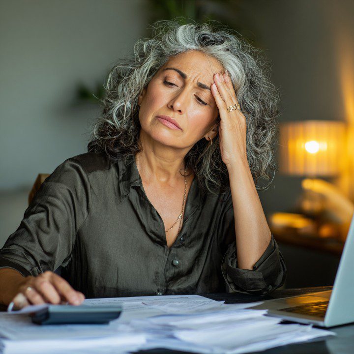 Middle-aged Latin American woman entrepreneur looking worried while reviewing financial documents at her desk.