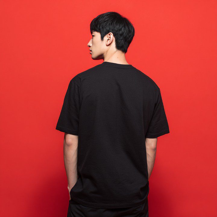 Back view of a young Korean man wearing a plain black oversized T-shirt against a vibrant red background.