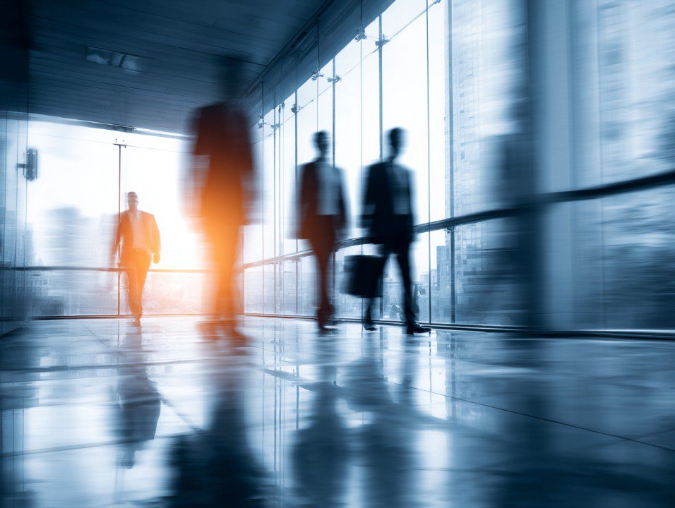 Motion blur image of business professionals walking in a modern glass office building.