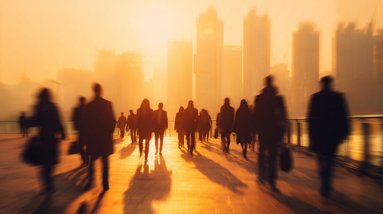 Silhouettes of commuters walking through a city in golden sunrise light with long shadows.