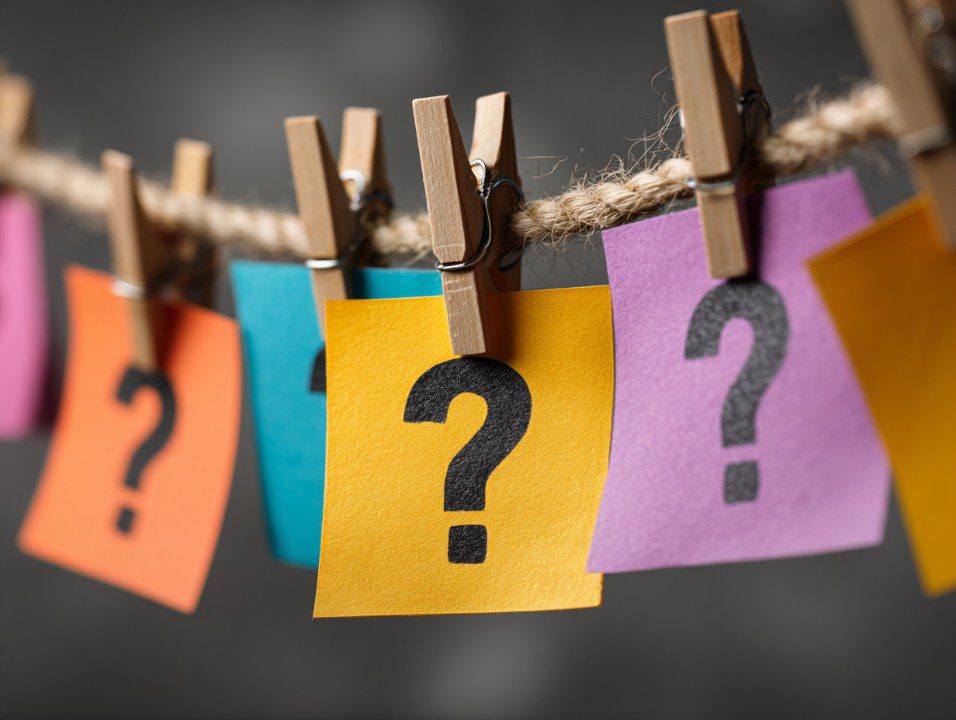 Brightly colored sticky notes with question marks, pegged to a rope with wooden clothespins, symbolizing curiosity.