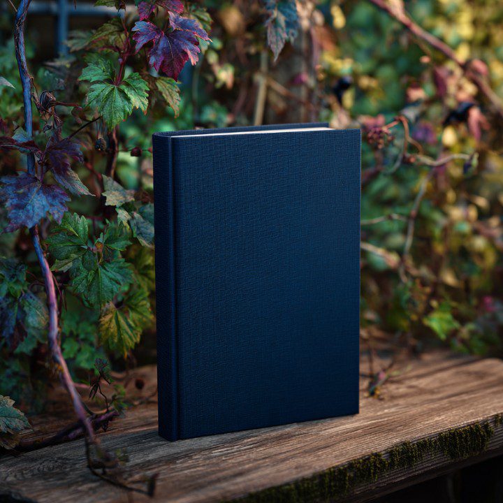 Dark blue hardcover book with blank cover on a wooden surface, surrounded by leafy plants, perfect for mockups and publishing visuals.