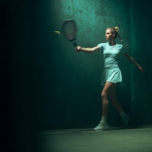 Female frontennis player mid-swing with a racket, in an editorial sports photo with moody green background.
