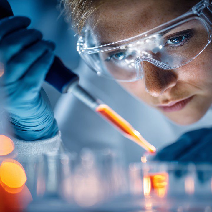 Female scientist in protective gear using a pipette for research in a modern laboratory.