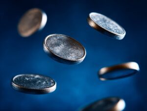 Close-up of multiple thin silver coins floating in mid-air against a blue background.
