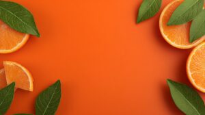 Flatlay of fresh orange slices with green leaves on a bright orange background.