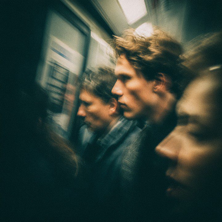 Motion-blurred street photograph of commuters in an underground subway station with a gritty, cinematic aesthetic.