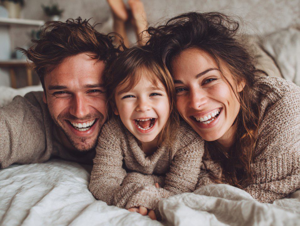 Smiling parents and child lying in bed together, enjoying a joyful morning.