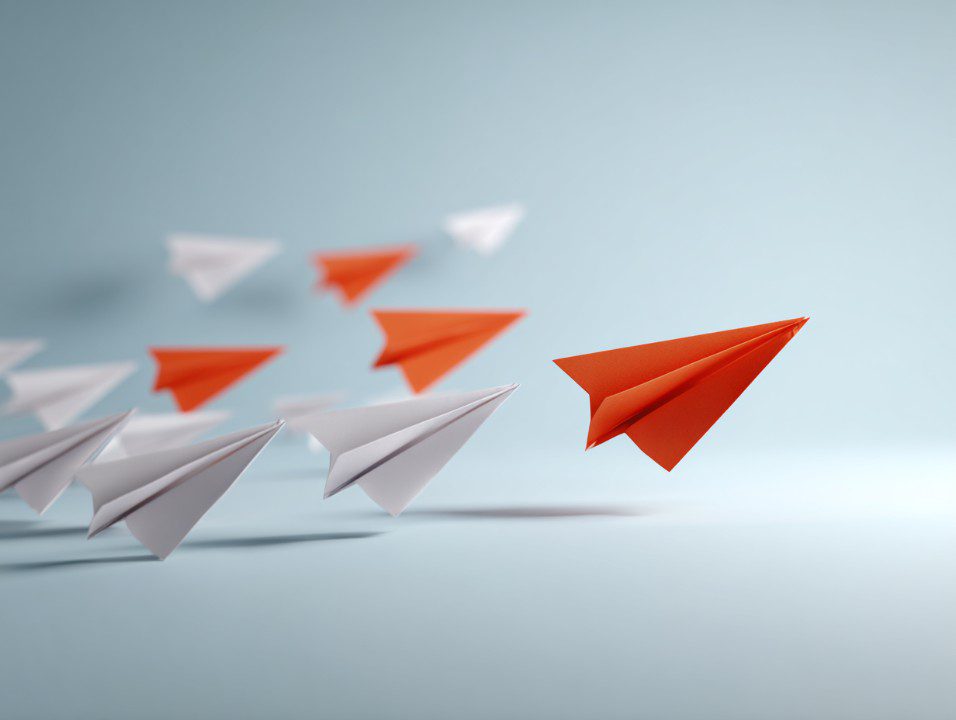Red paper airplane leading a group of white airplanes in a symbolic concept of leadership and innovation.