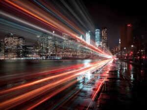 Long-exposure photograph of Manhattan skyline with light streaks and reflections on wet streets.