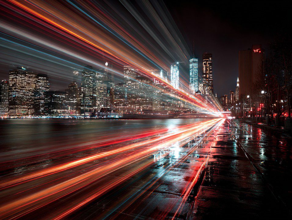 Long-exposure photograph of Manhattan skyline with light streaks and reflections on wet streets.