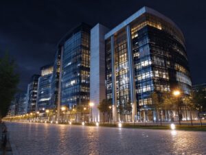 Modern glass office building in Paris illuminated at night with cobblestone street and streetlights.