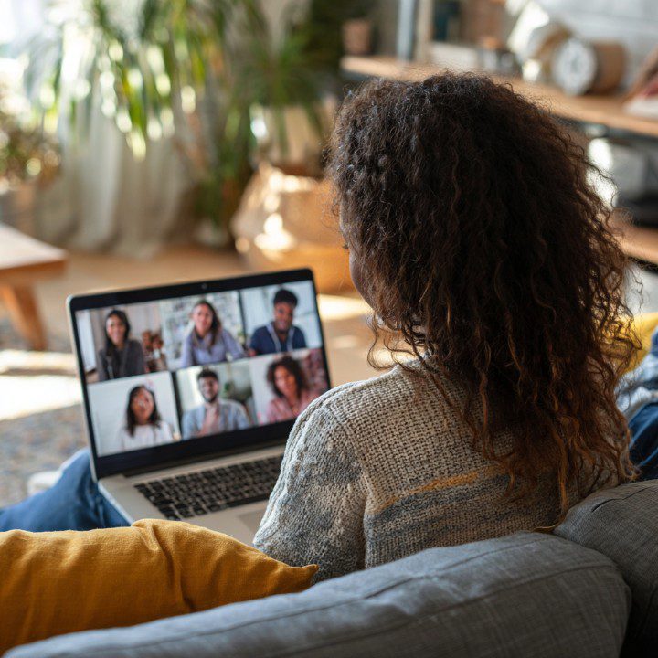 Woman participating in an online group video meeting from home using a laptop.