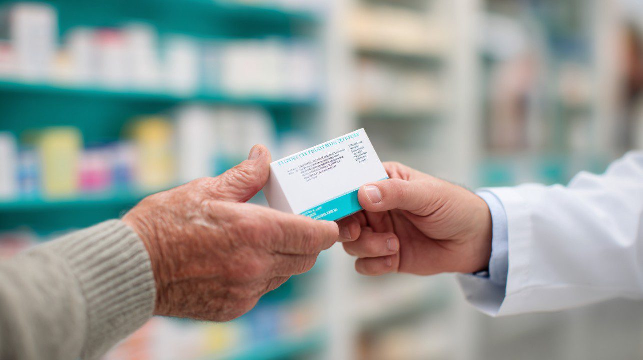 Close-up of a pharmacist handing a prescription medication box to a patient in a modern pharmacy setting.