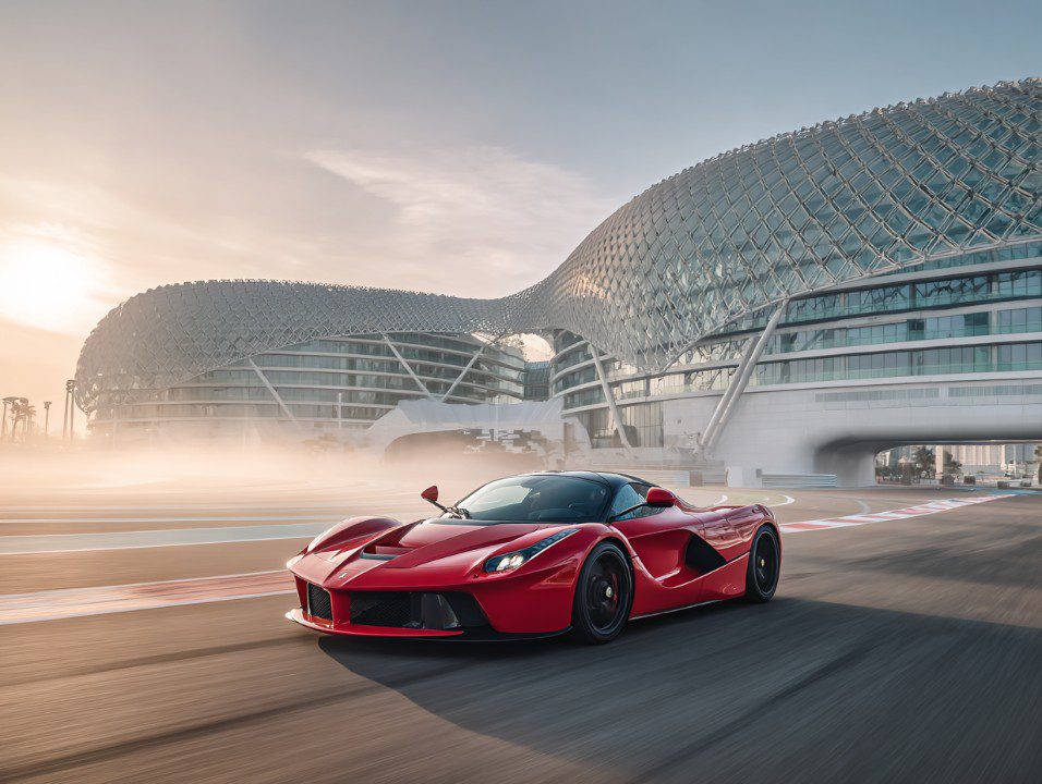 Red Ferrari LaFerrari racing on the Abu Dhabi Yas Marina Formula 1 track with the futuristic Yas Hotel in the background at sunrise.