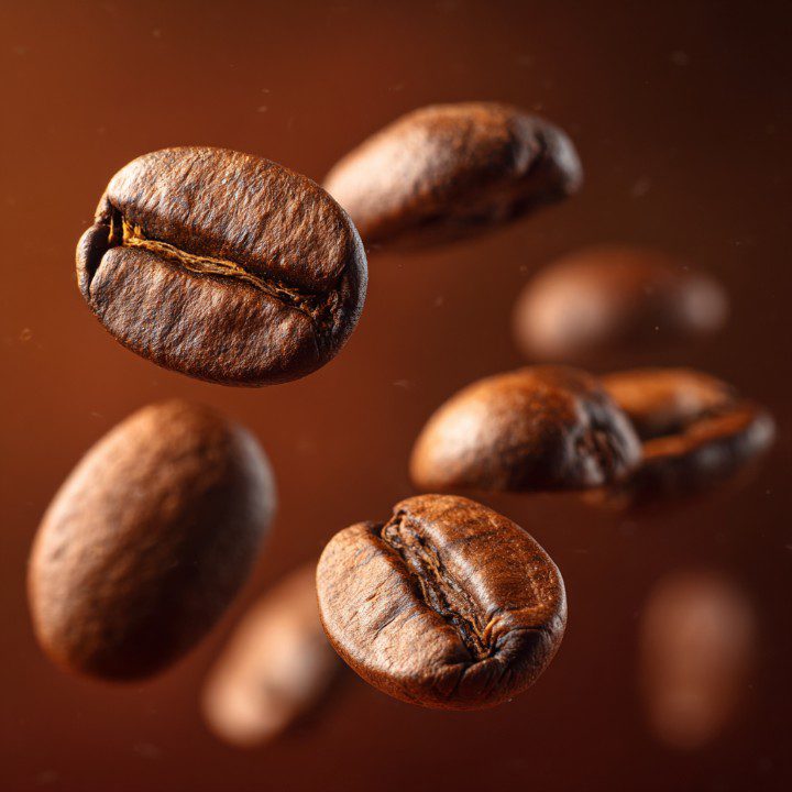 Close-up of roasted coffee beans floating in mid-air with a brown background.