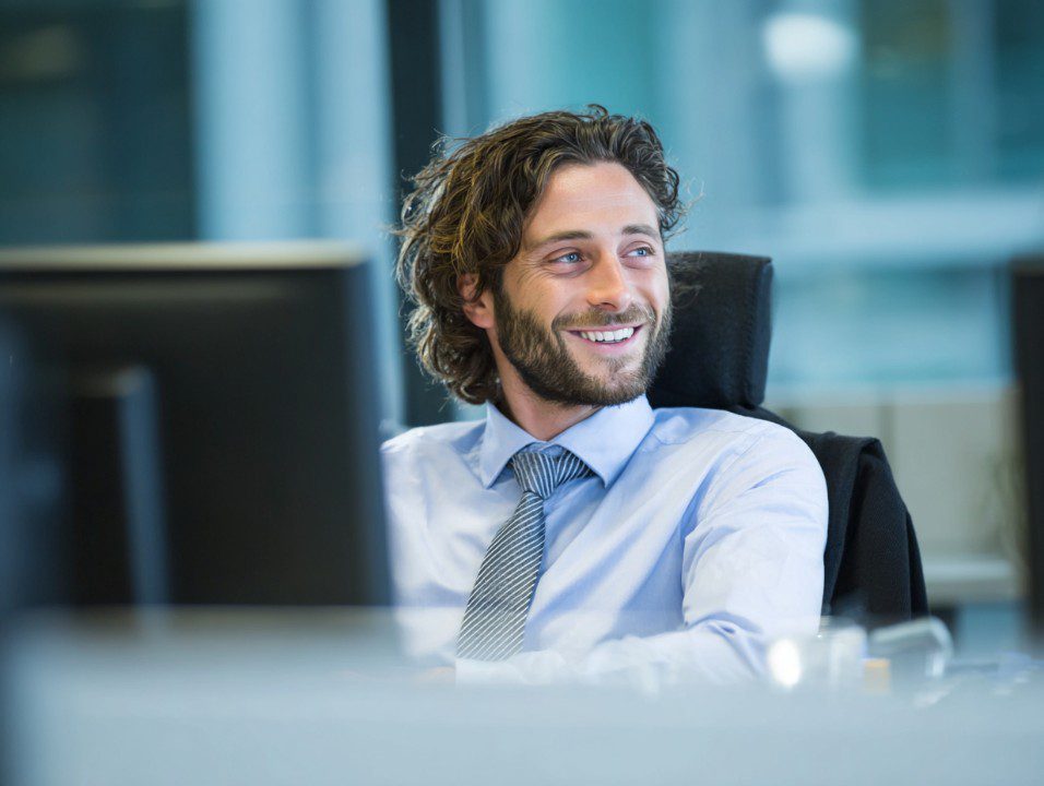 Businessman with curly hair and beard smiling during an office discussion.