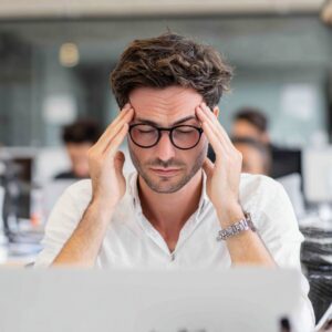 Man in glasses holding his temples in stress while working in an office environment.